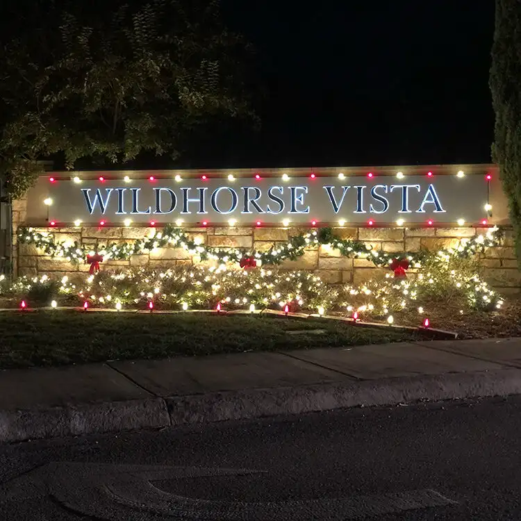 Wildhorse Vista neighborhood entrance sign lit with Christmas lights, garland, and red bows at night