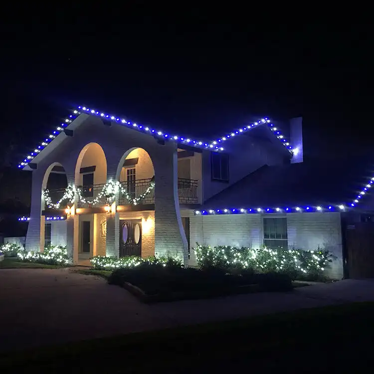 Two-story white brick home outlined in blue and white roofline Christmas lights at night