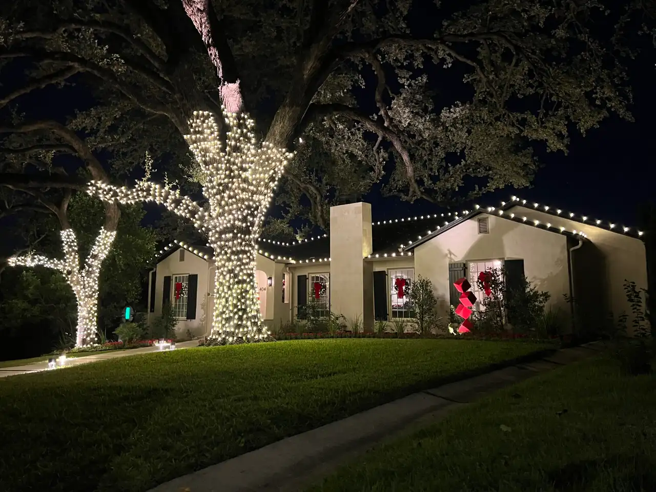 Warm white roofline Christmas lights and wrapped oak trees on stucco home at night