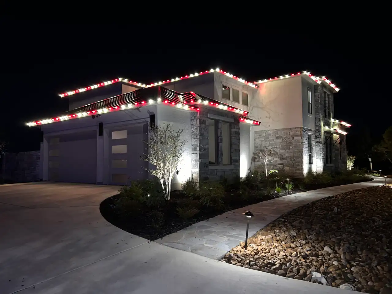 Red and white C9 Christmas lights outlining roofline of modern stone home at night
