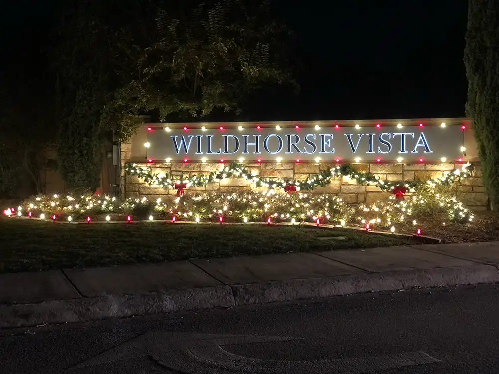 Wildhorse Vista neighborhood entrance sign lit with holiday lights, garland, and red bows at night