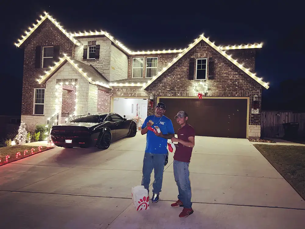 Two installers in driveway after finishing warm white roofline Christmas lights on brick home