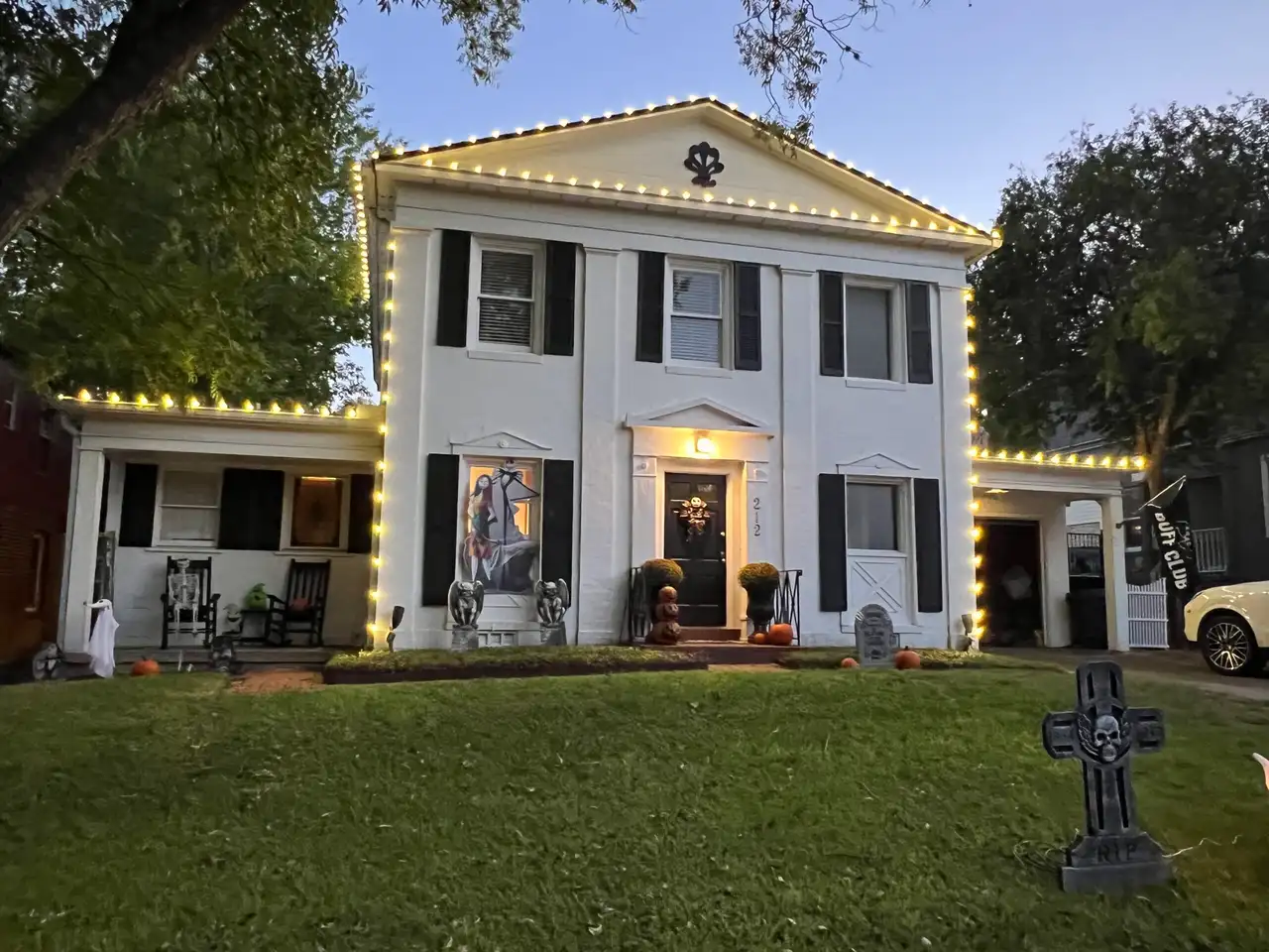 Warm white C9 roofline lights on white two-story home with Halloween yard decorations