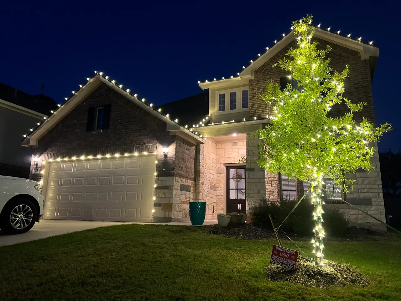 Warm white C9 roofline lights on brick home with lit front yard tree at dusk