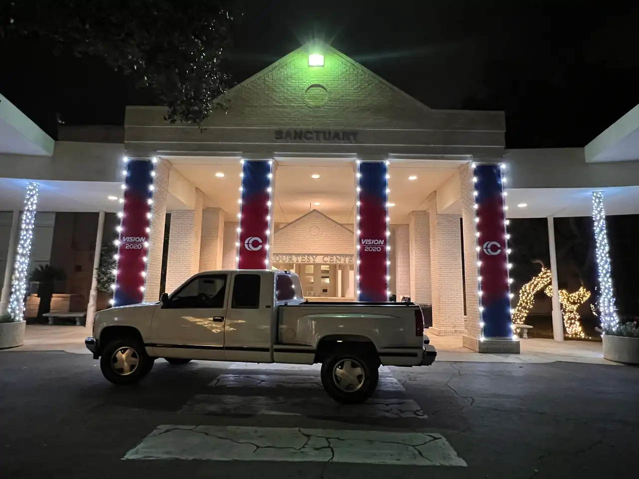 White string lights wrapped around church sanctuary columns at night with work truck parked outside